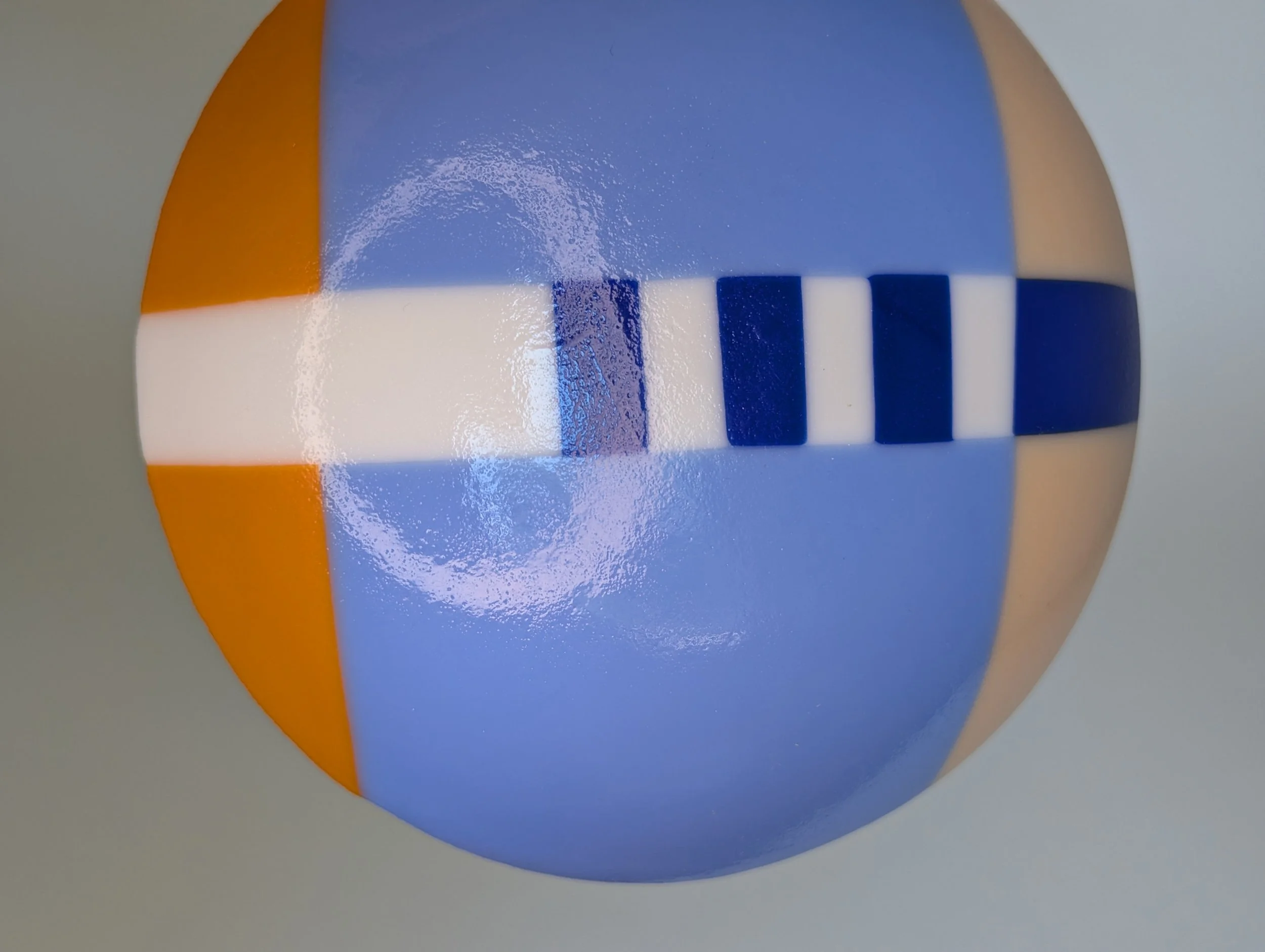 Circular glass bowl with geometric patterns in blue, orange, and white set on a plain light background.
