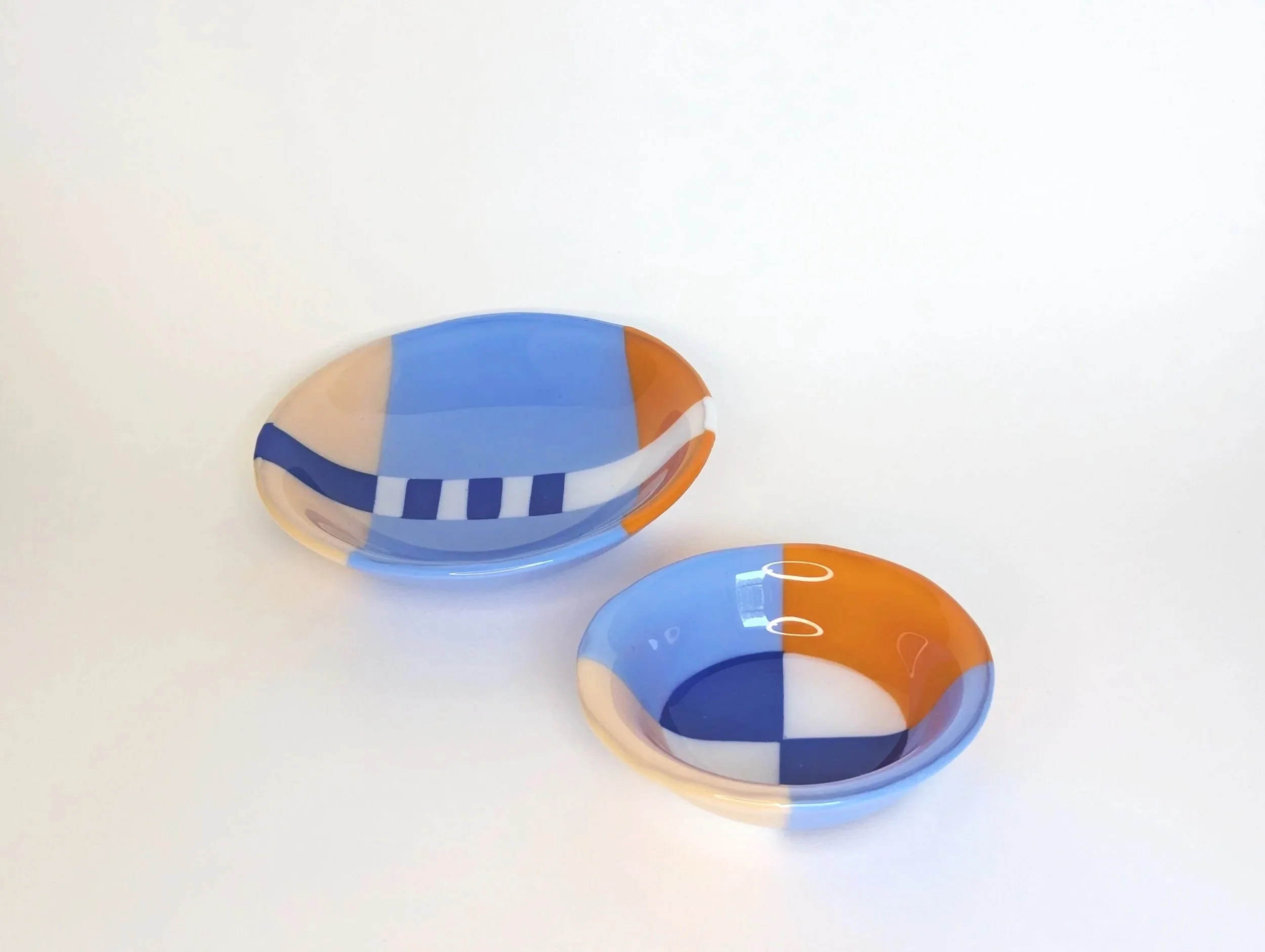 Two circular glass bowls with geometric patterns in blue, orange, and white set on a plain light background.