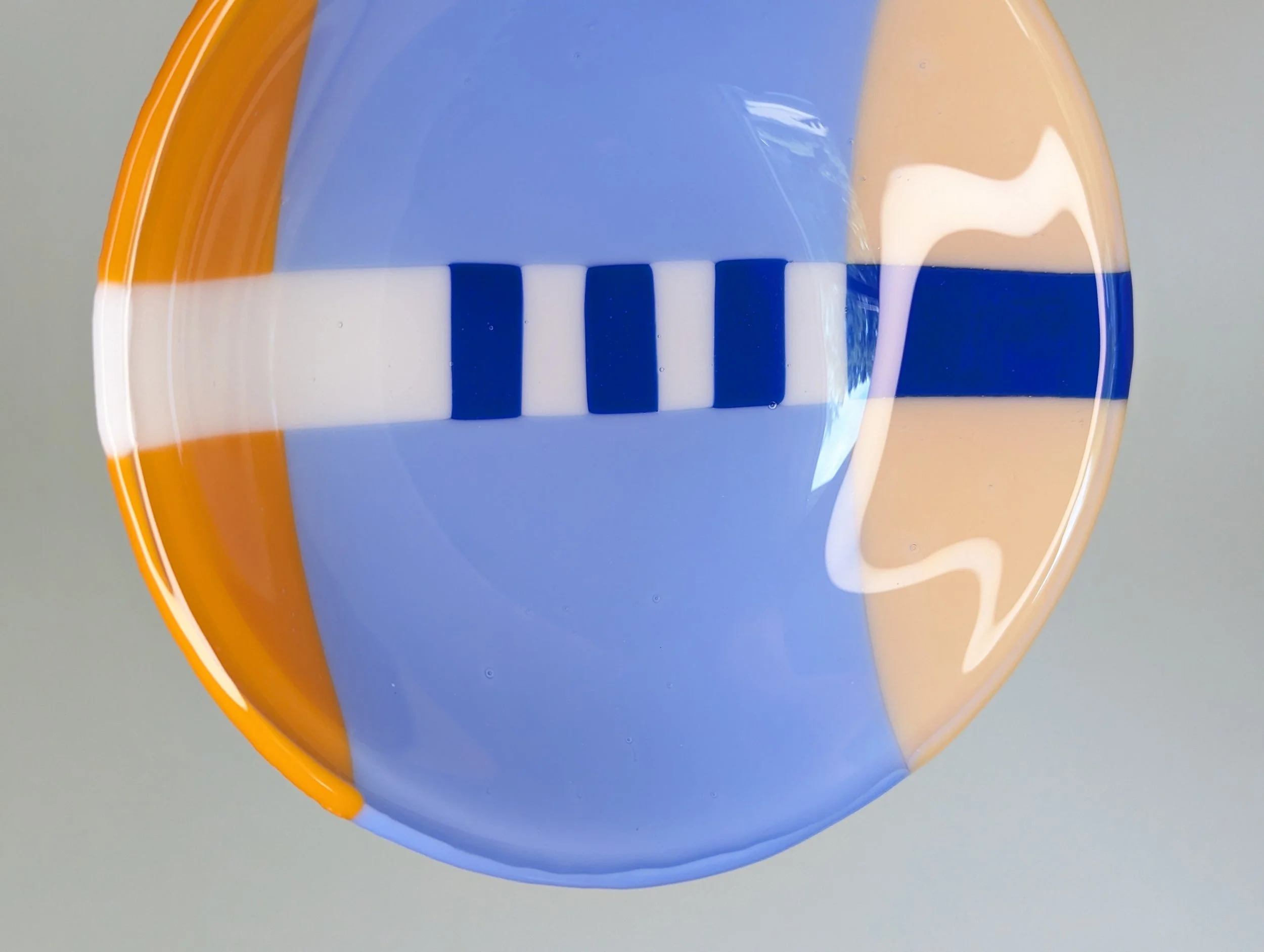 Circular glass bowl with geometric patterns in blue, orange, and white set on a plain light background.