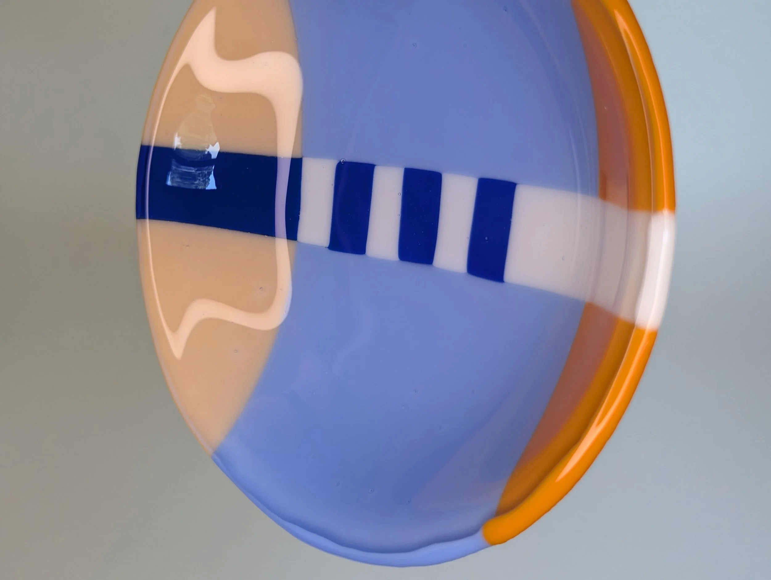 Circular glass bowl with geometric patterns in blue, orange, and white set on a plain light background.