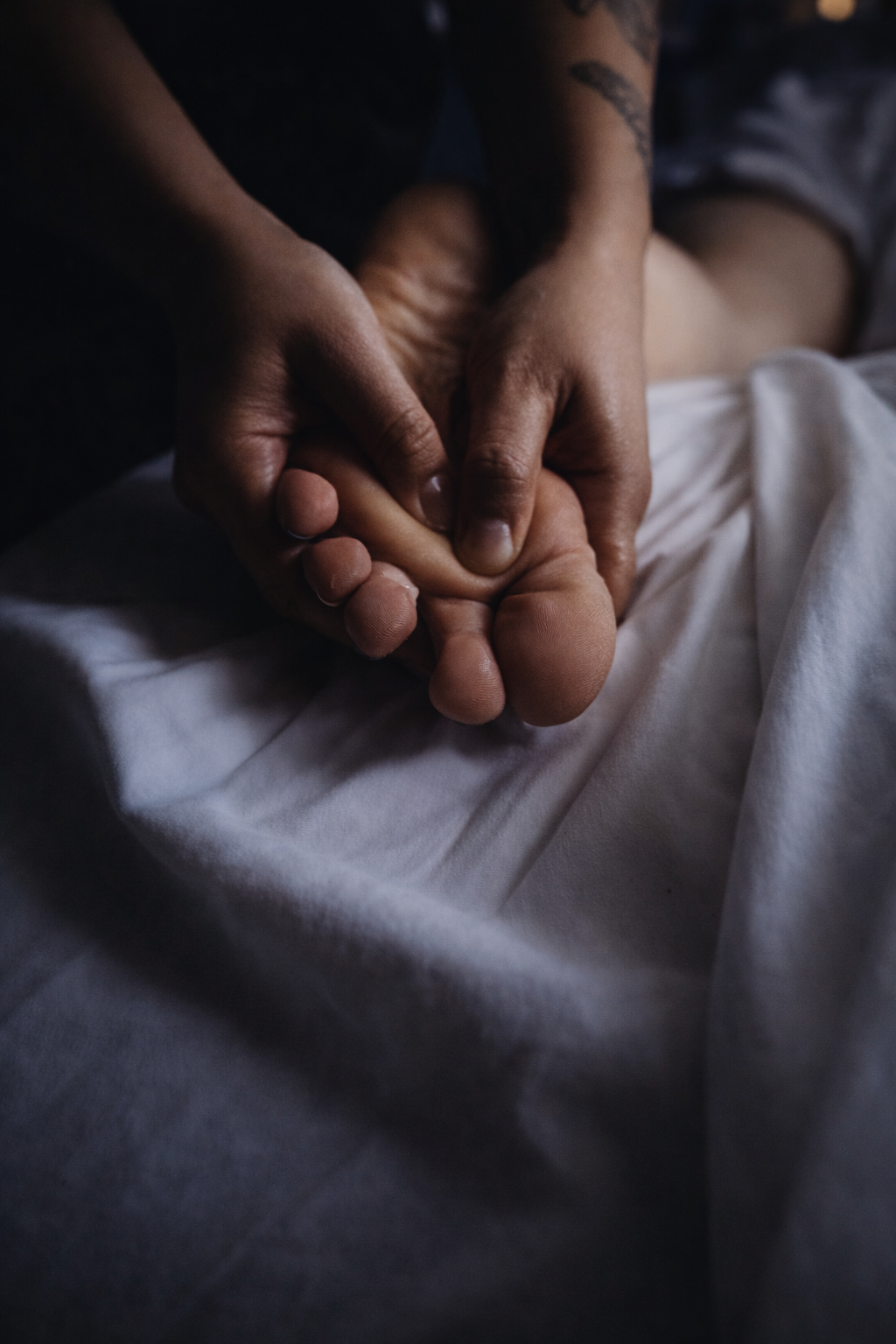Close-up of two hands gently holding a newborn baby's foot, lying on a white blanket.