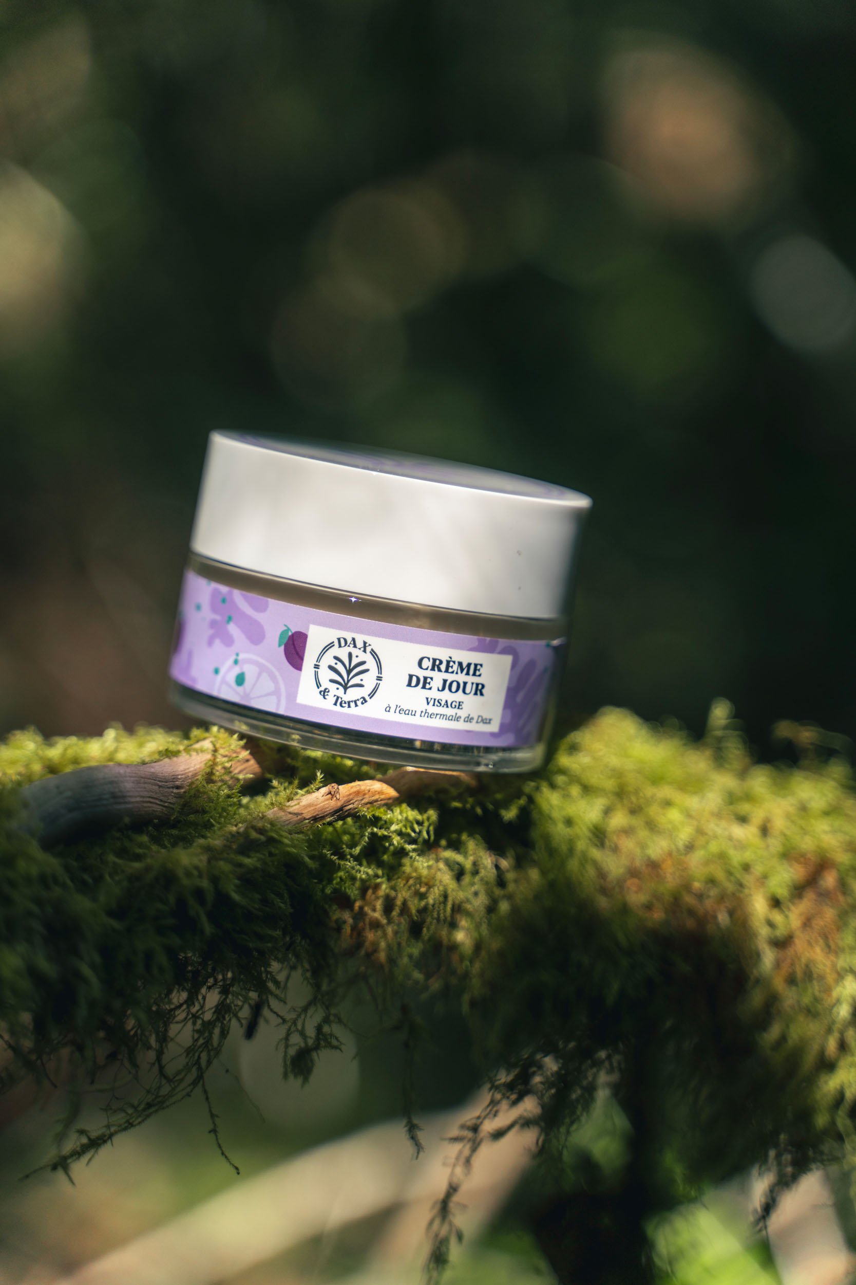 A small jar of DAX Terra Crème de Jour face cream resting on a moss-covered tree branch in a forest setting.