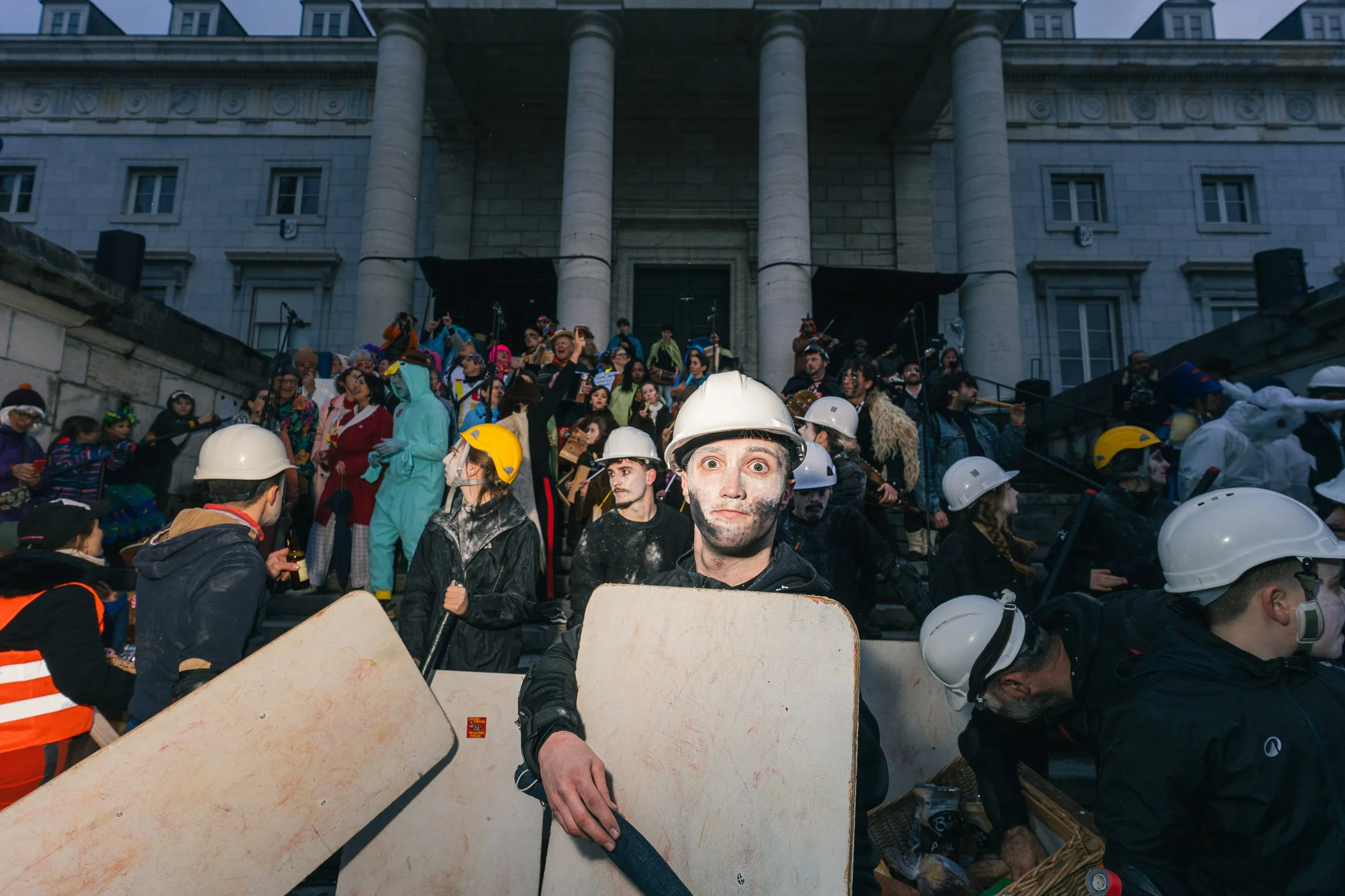 Protesters in hard hats and masks on steps of a government building during a demonstration.