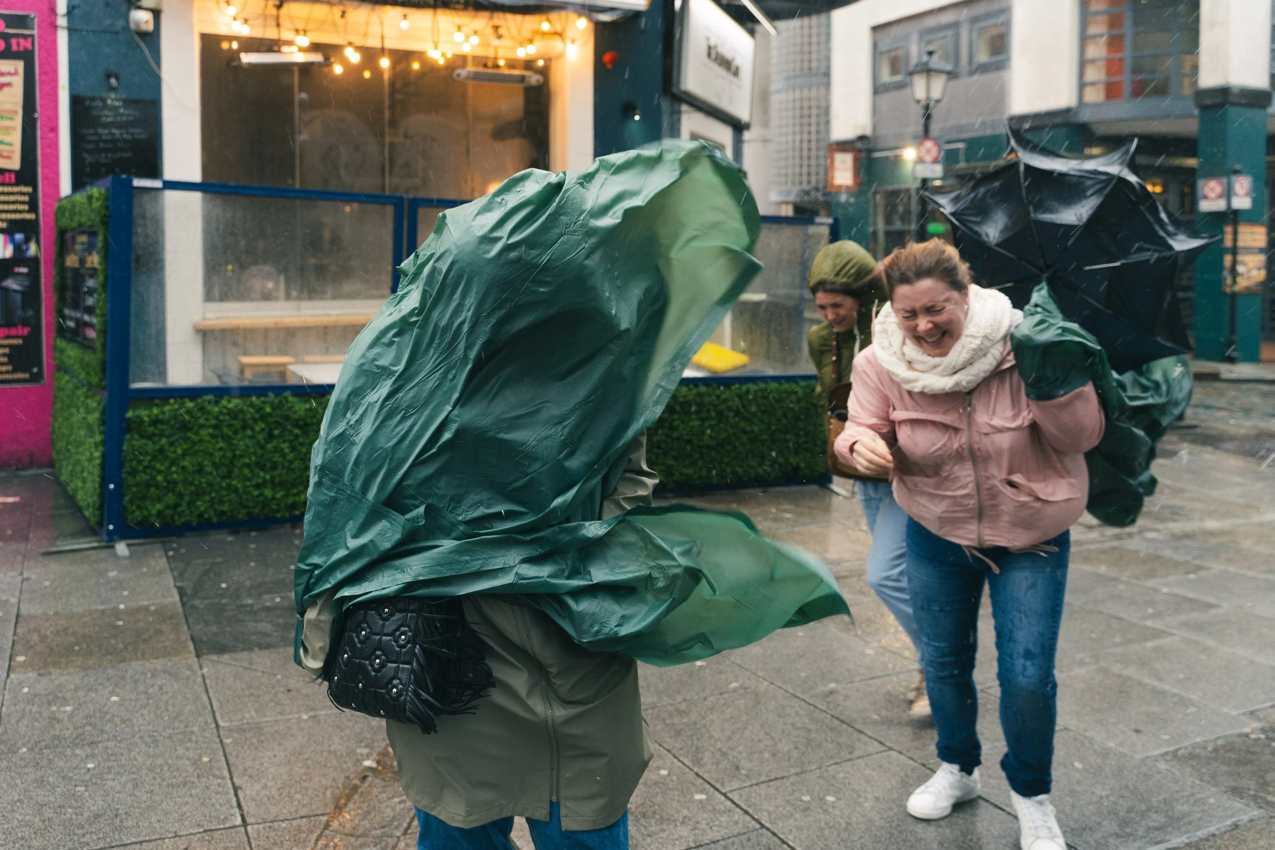 Two women laughing and having fun with umbrellas in the rain on a city street.