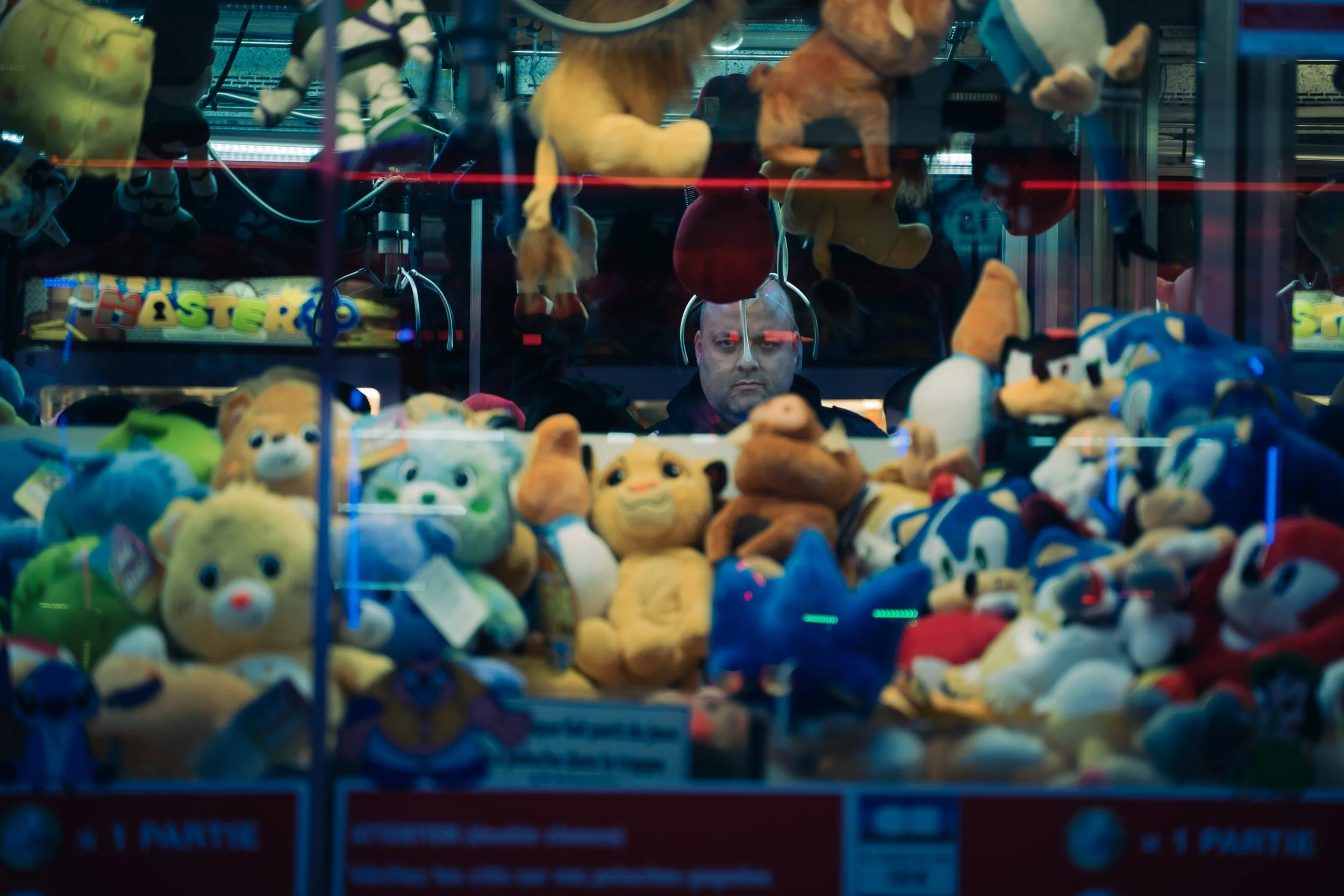 A person behind a glass-fronted claw machine filled with various plush toys including animals and cartoon characters. The person appears focused on the game.