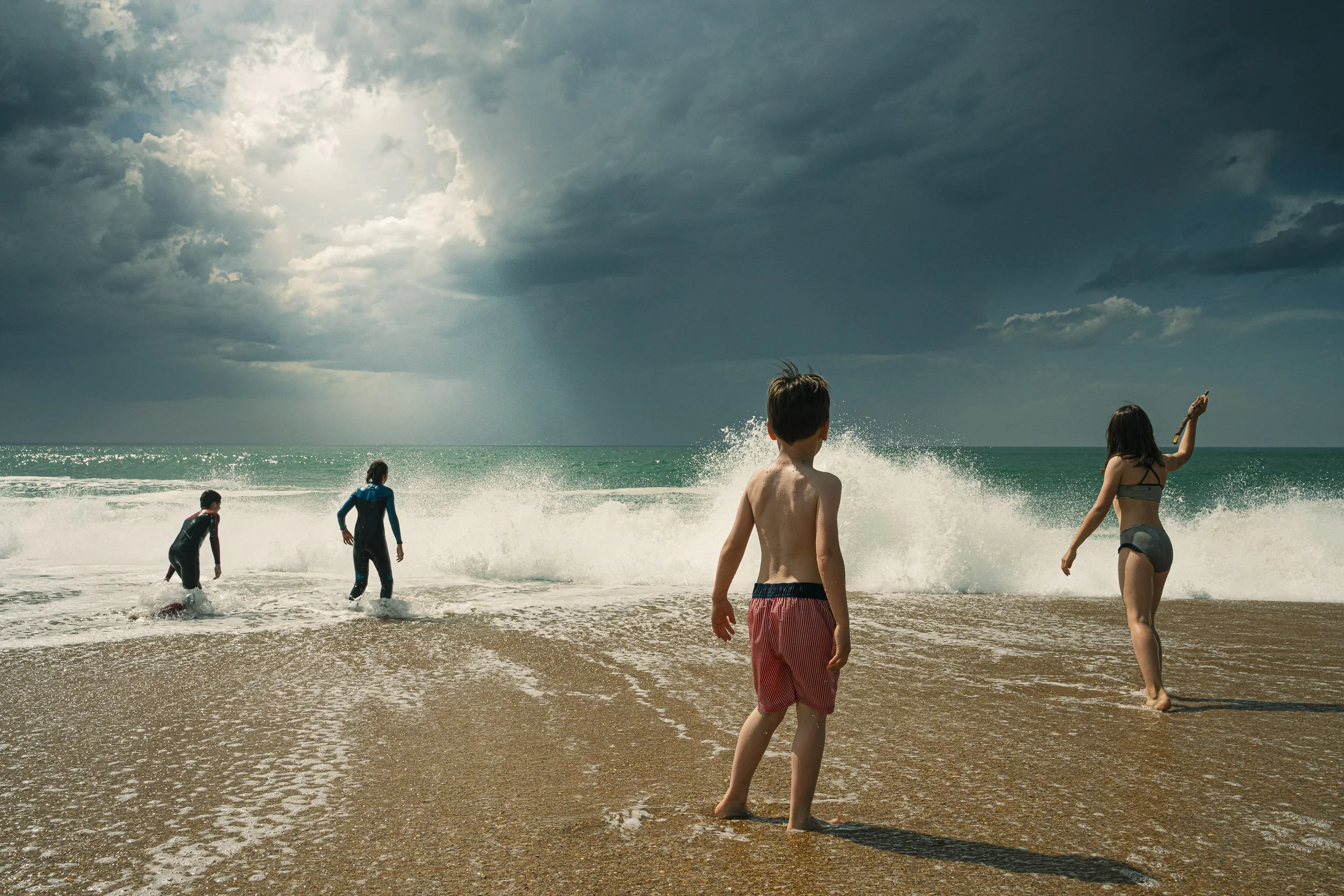 Children playing at the beach near the ocean on a cloudy day.