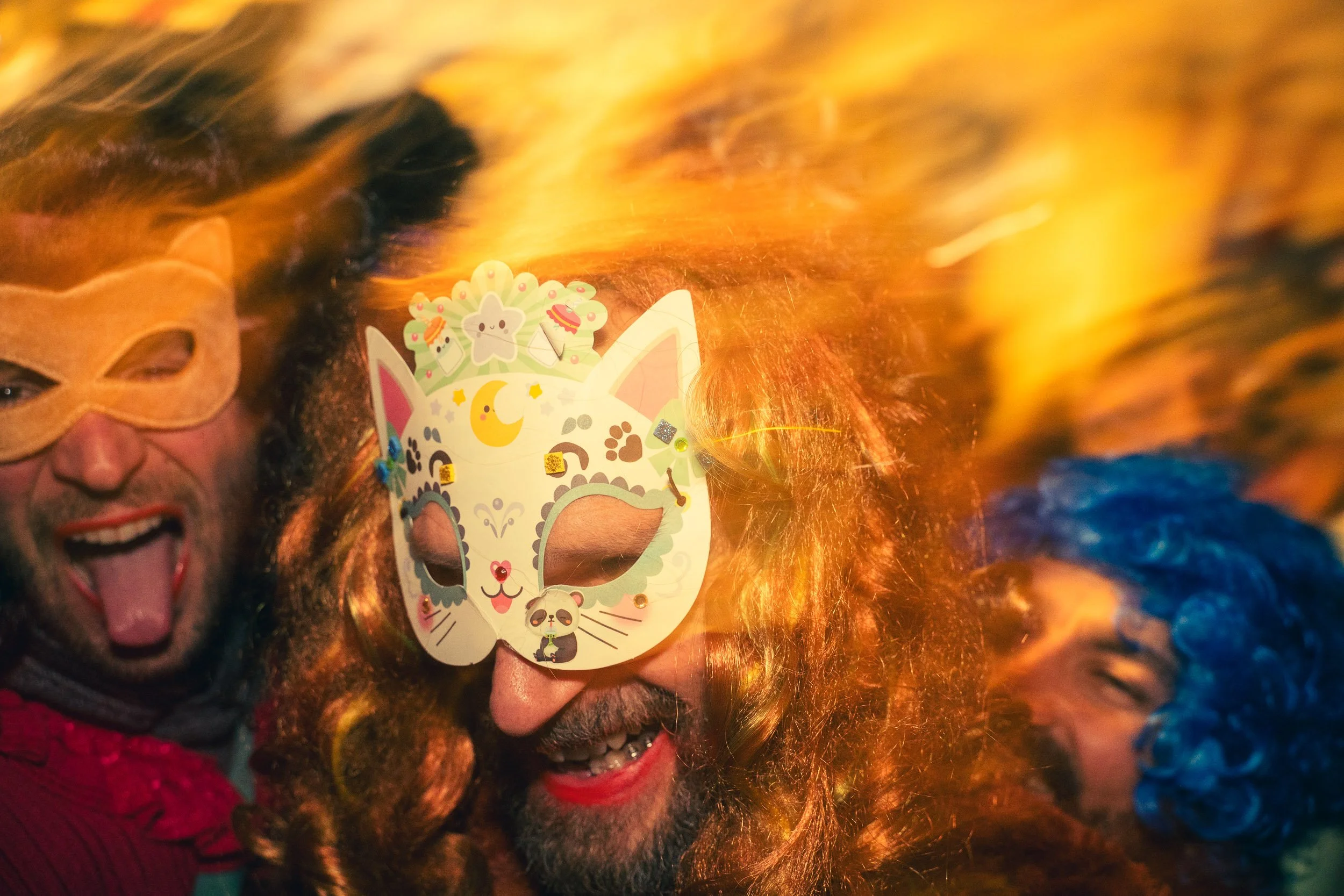 People celebrating at a costume party, wearing colorful masks and wigs, with festive expressions and joyful mood.