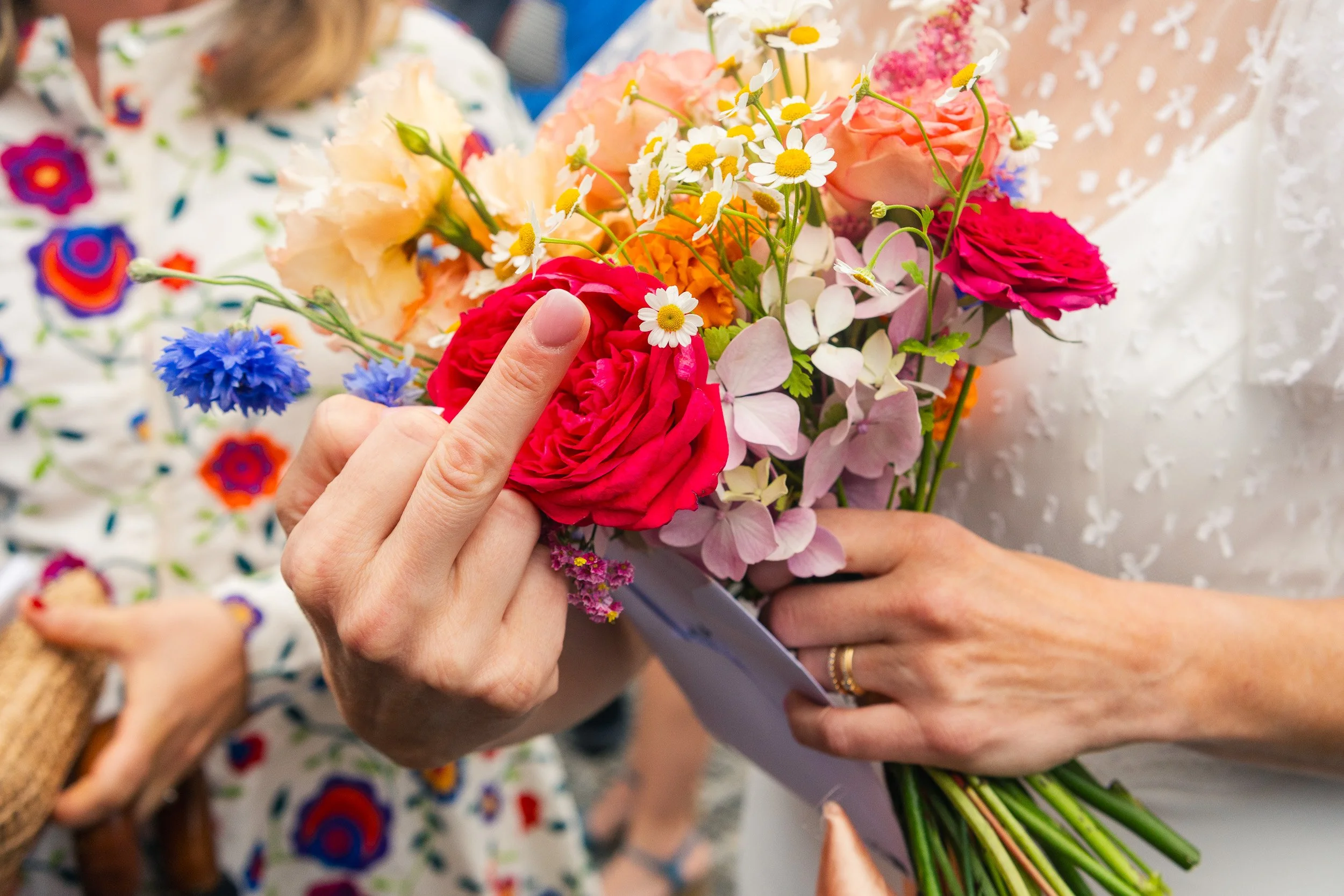Close-up of a person holding a colorful bouquet of various flowers including roses, daisies, hydrangeas, and other blooms, with their middle finger raised.