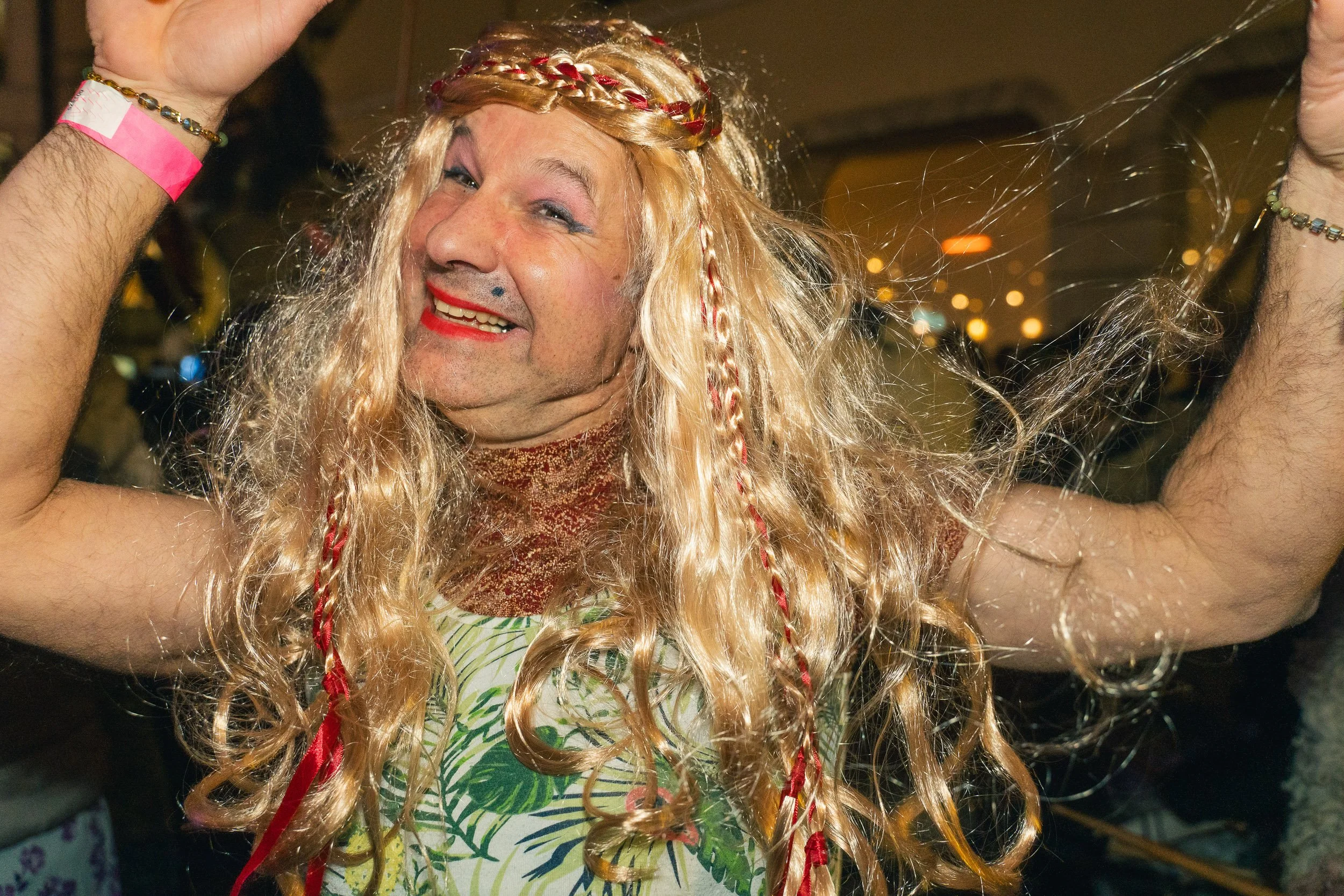 Person with long blonde hair dressed in a colorful outfit, smiling and dancing at a lively party.