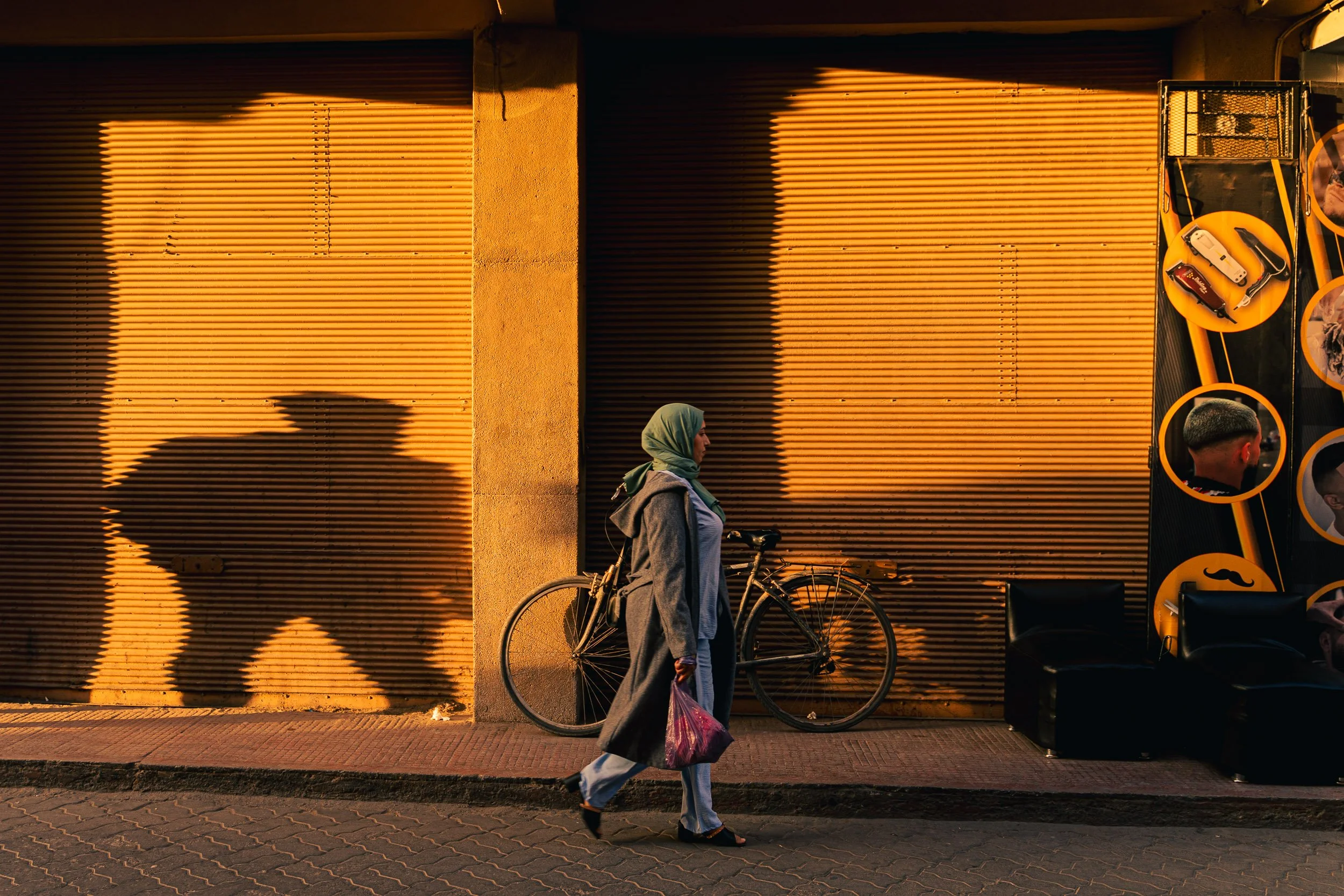 Une femme voilée se balade dans les rues de Taroudant au Maroc au coucher de soleil. Une ombre masculine la suit. Elle passe devant un magasin de coiffure