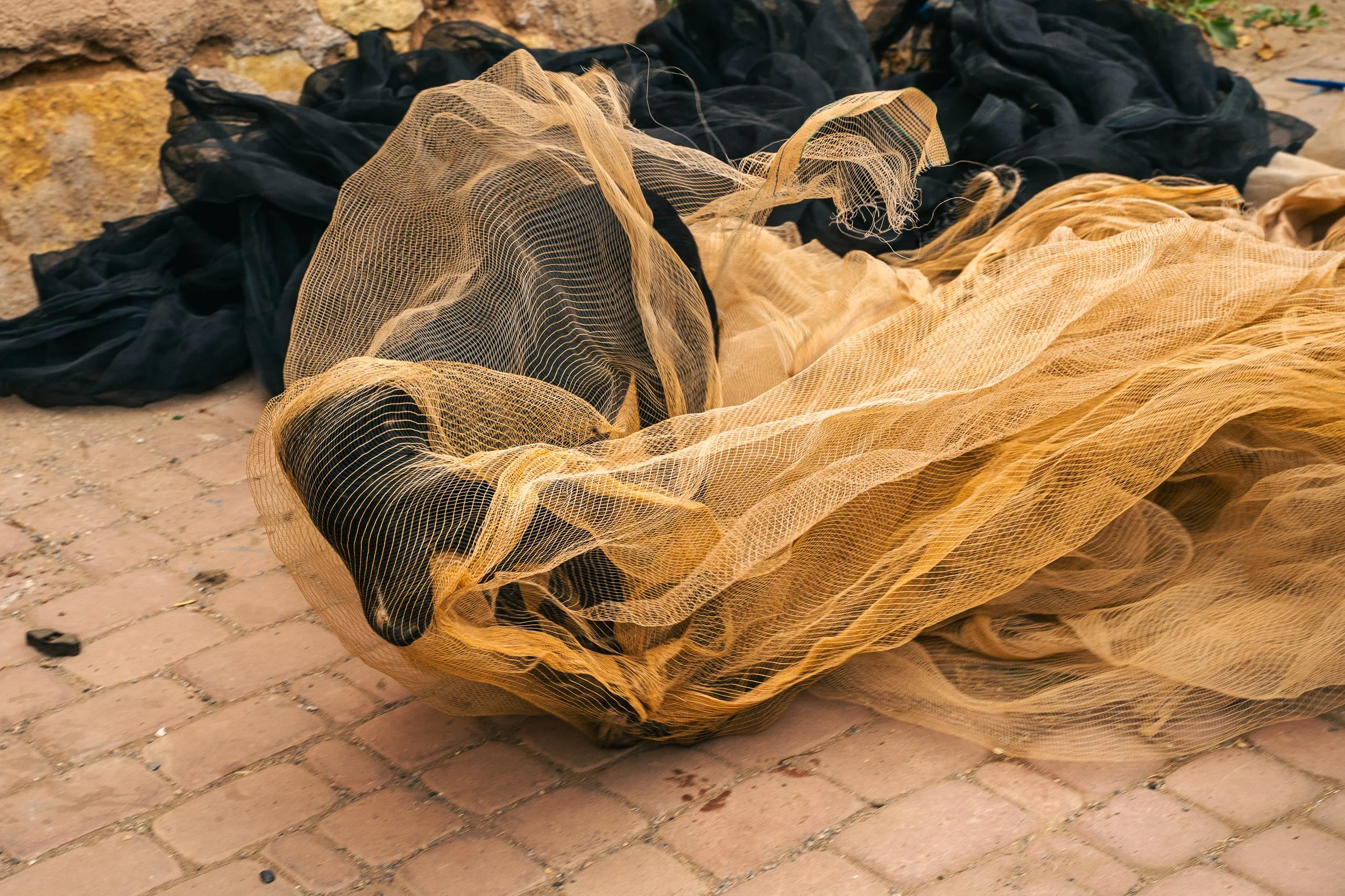 A pile of black and yellow fishing nets laid on a brick pavement.