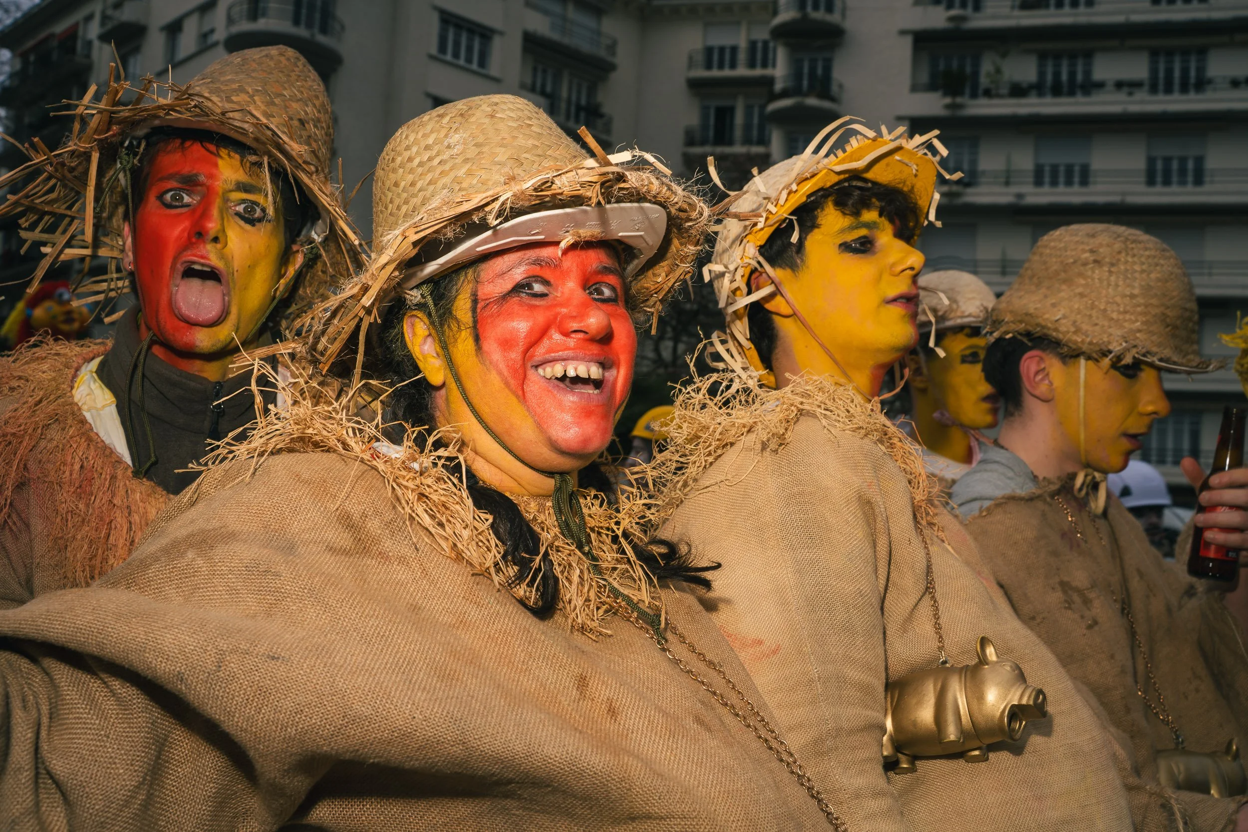 People dressed in costumes with straw hats and face paint, participating in a street parade or celebration in an urban setting.