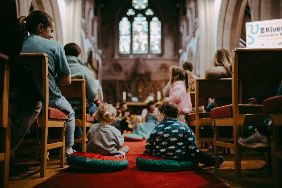 Children and adults seated on cushions and chairs inside a church during a storytelling event.