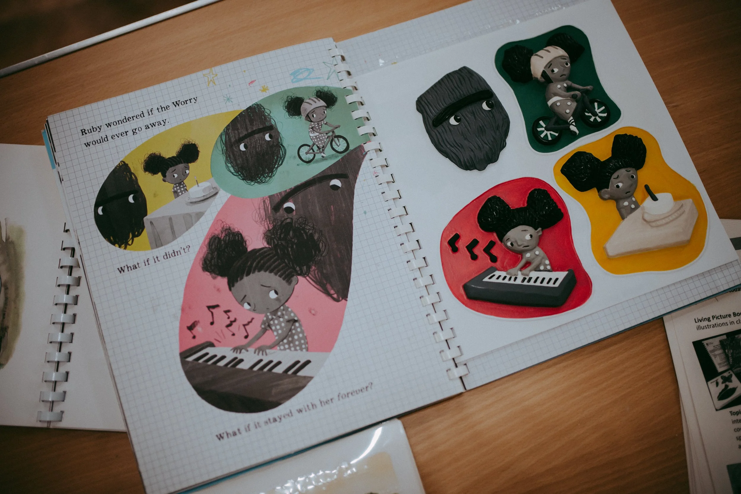 A children's activity book shows illustrations of a girl with curly hair, a girl with pigtails, and a girl with blond hair, along with 3 different textured and shaped clay or plasticine figures of a girl with pigtails riding a bicycle, a girl with pi