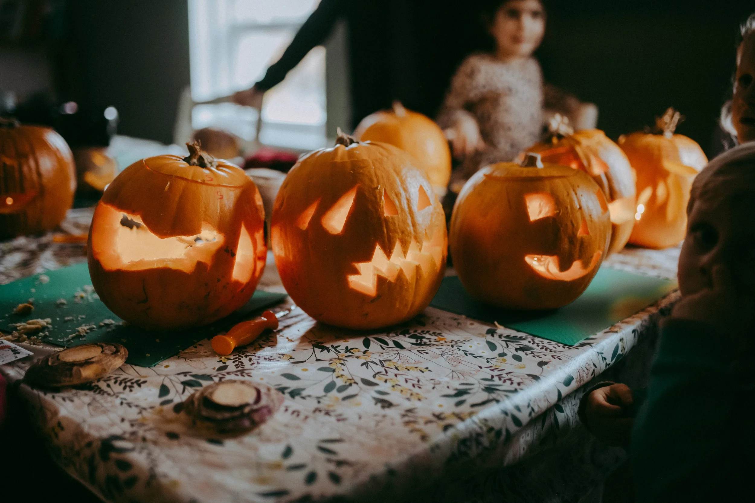 Several carved pumpkins with candlelight inside on a table with a Halloween-themed tablecloth.