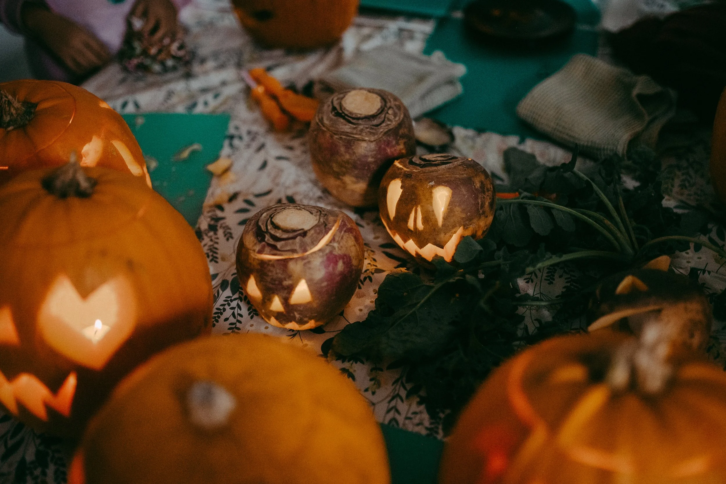Close-up of carved pumpkins with candles inside, on a table with decorations and cloth, creating a Halloween setting.