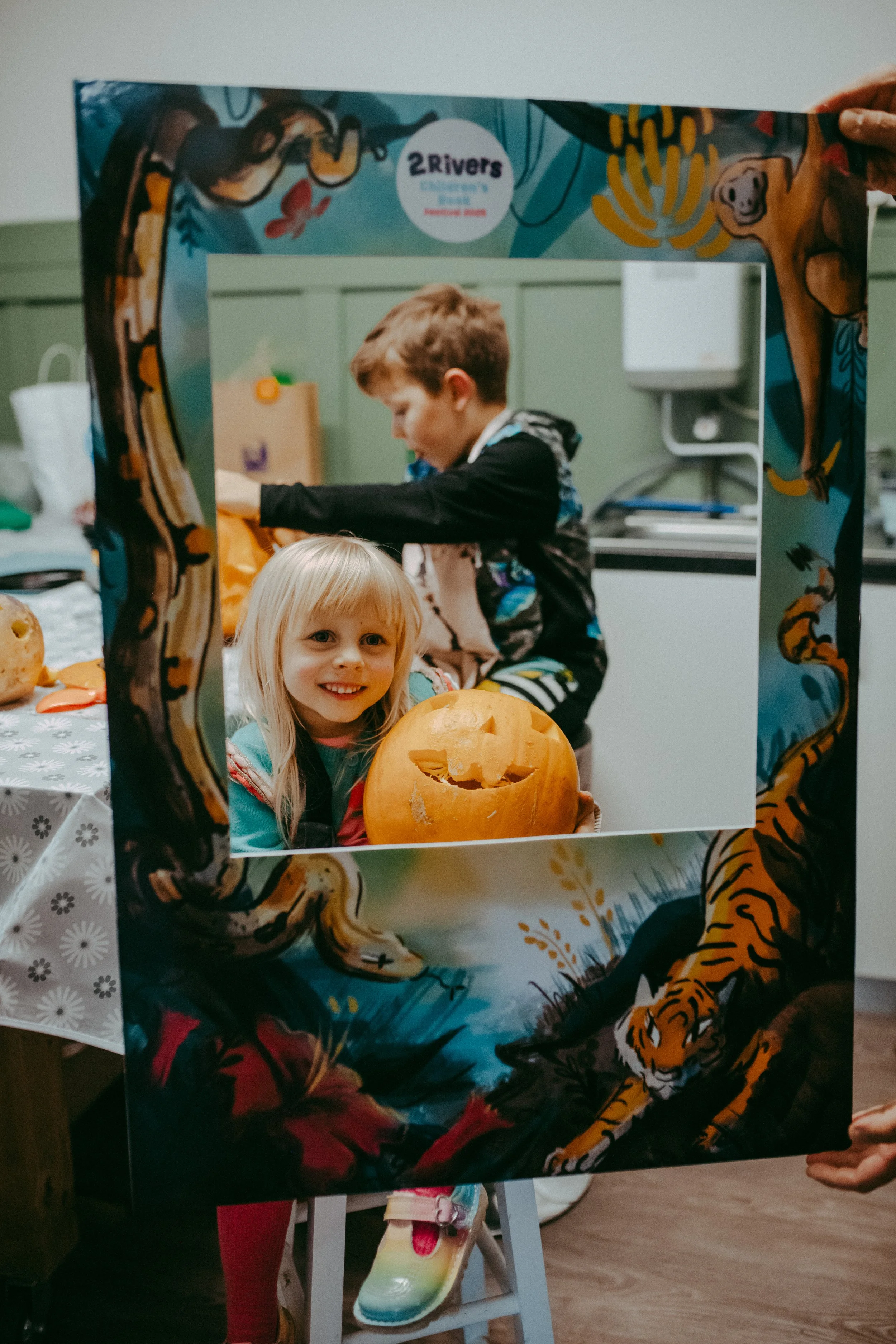 Children with a pumpkin at a book event with a tiger and jungle-themed selfie frame.