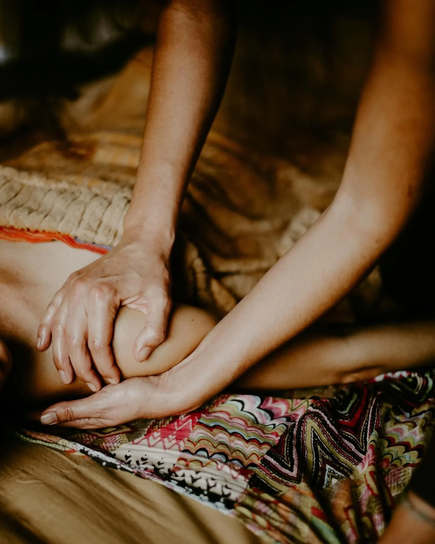 Hands giving a massage on a person's back, with the person lying face up, wearing patterned clothing.