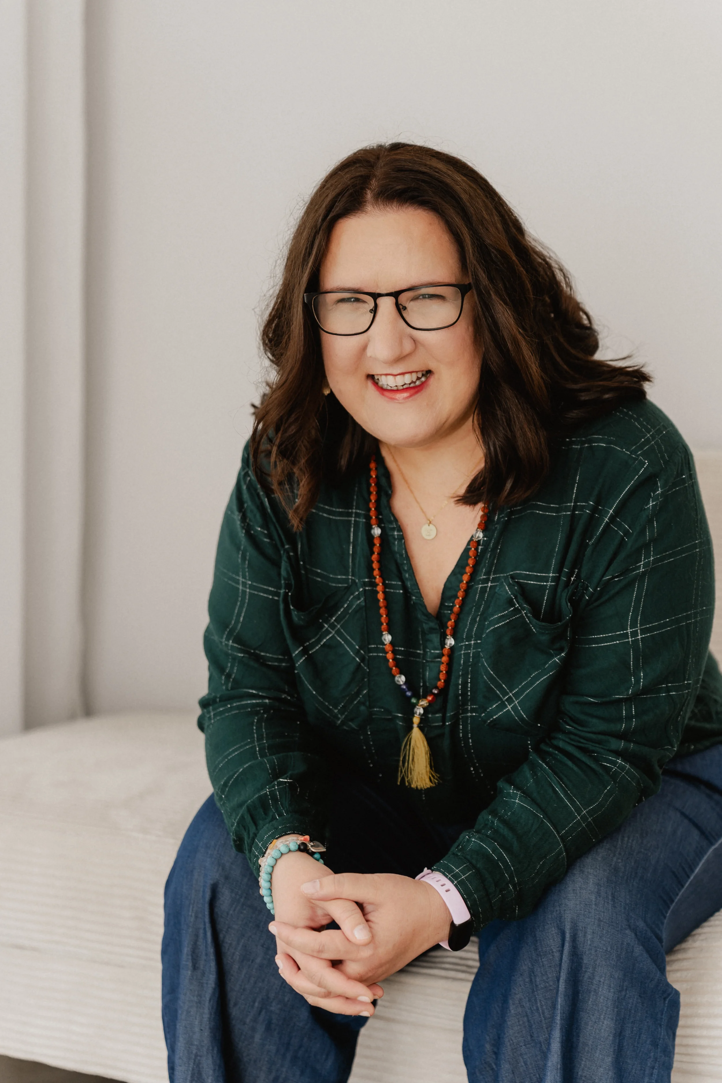 Barbara Dilsiz mit braunen Haaren, Brille und grüner Bluse sitzt auf einer weißen Couch.