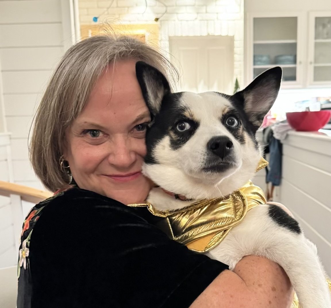 A woman holding a black and white husky puppy with blue eyes, both smiling in a cozy kitchen.