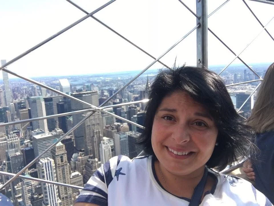 A woman taking a selfie on a rooftop of a skyscraper, with the New York City skyline in the background.