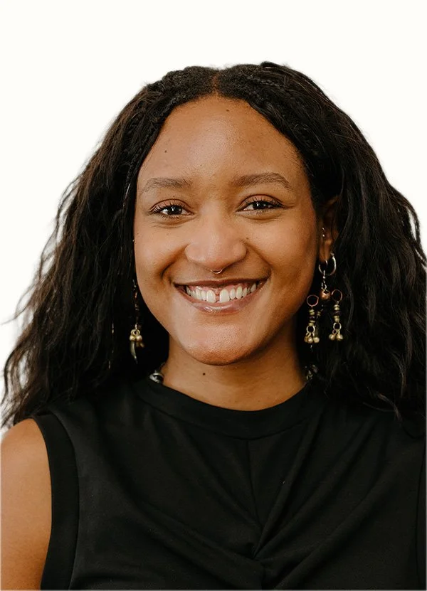 A woman with dark, curly hair smiling at the camera, wearing a black sleeveless top and dangling earrings.