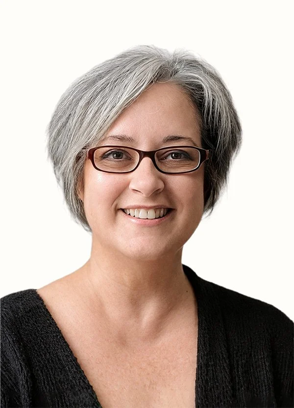 A woman with short gray hair, glasses, and a black top, smiling against a plain white background.