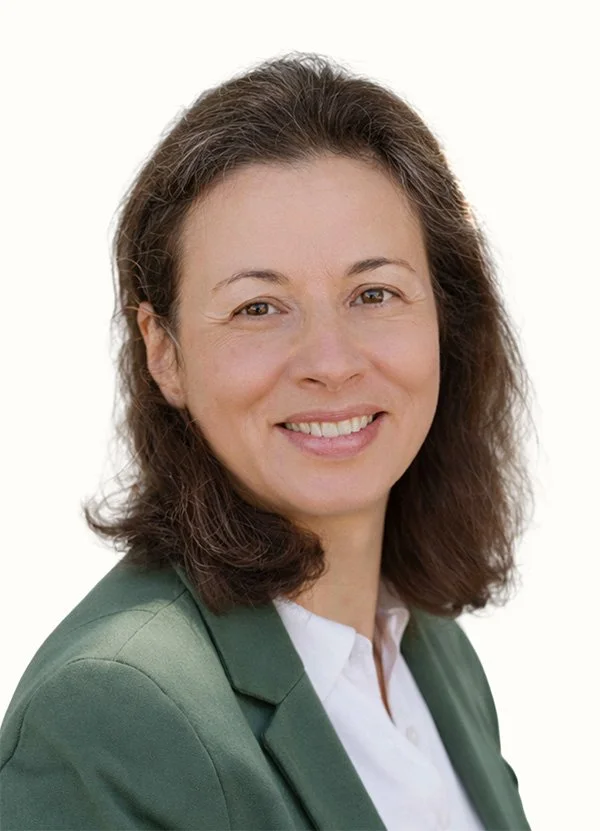 Portrait of a woman with shoulder-length brown hair, wearing a white blouse and green blazer, smiling at the camera.