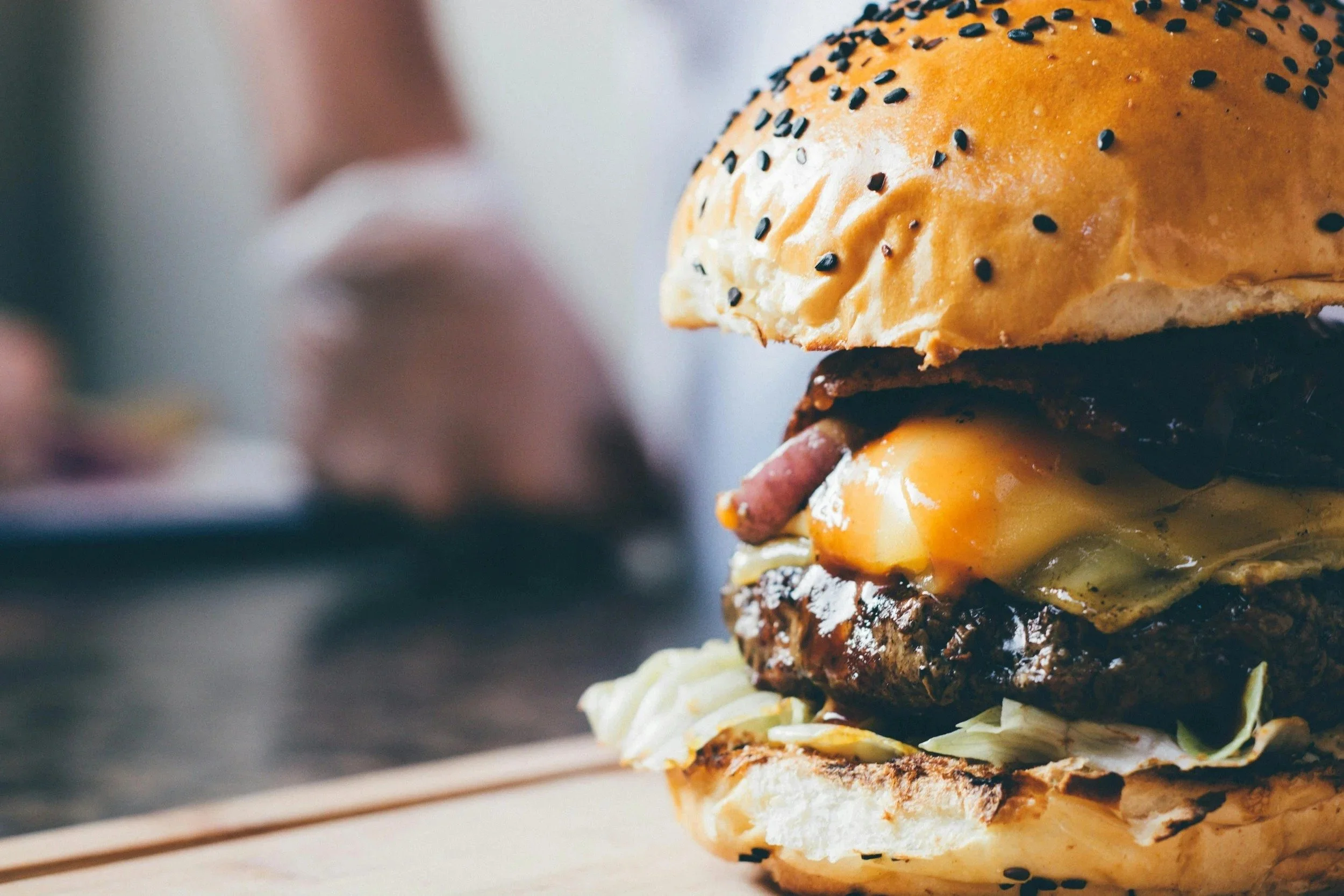Close-up of a veggie burger with lettuce, patty, melted cheese, and a seed bun.
