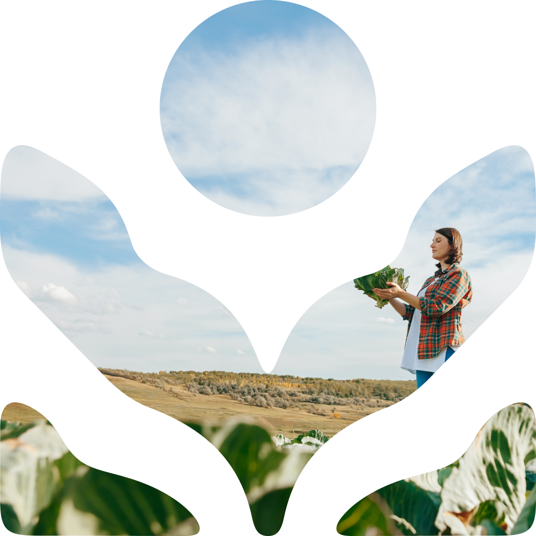 A woman holding a bunch of leafy greens outdoors with a cloudy sky and open field in the background.