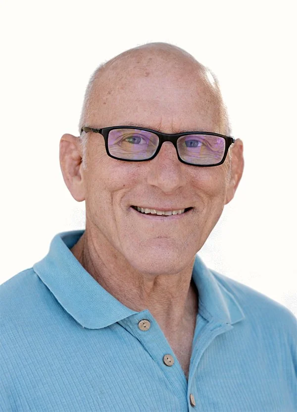 Portrait of a smiling older man with glasses and a light blue polo shirt against a white background.