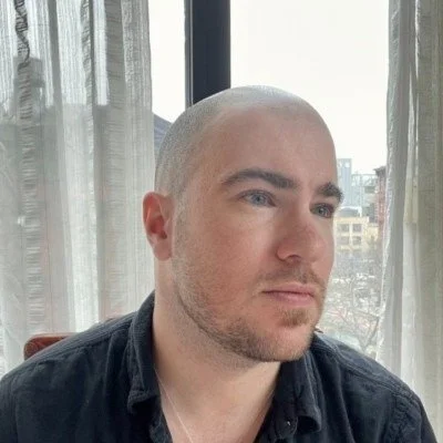 A man with a shaved head and light skin looking out a window.