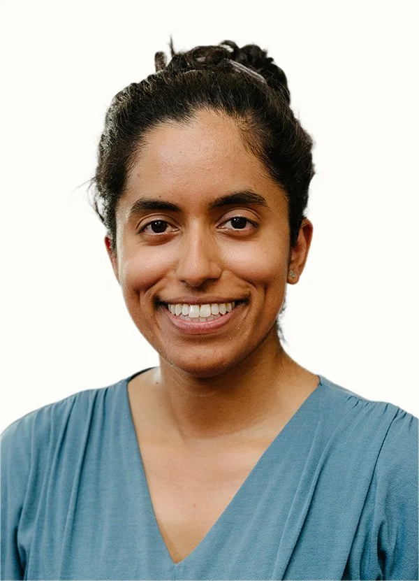 Portrait of a smiling woman with her hair pulled back, wearing a teal blouse against a white background.
