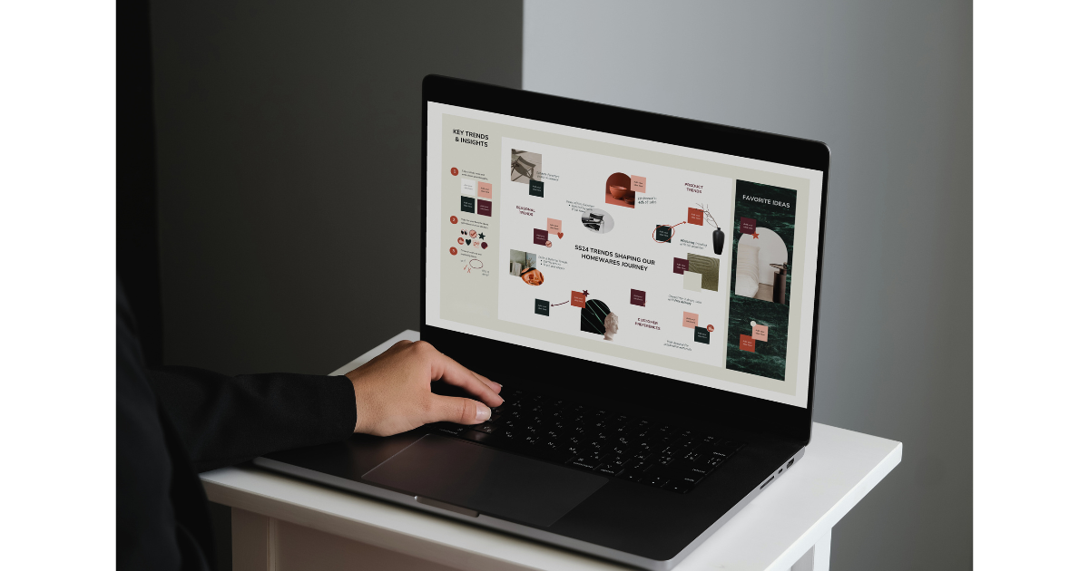 Person using a black laptop on a white desk, displaying a presentation or infographic on trends in homeware design.