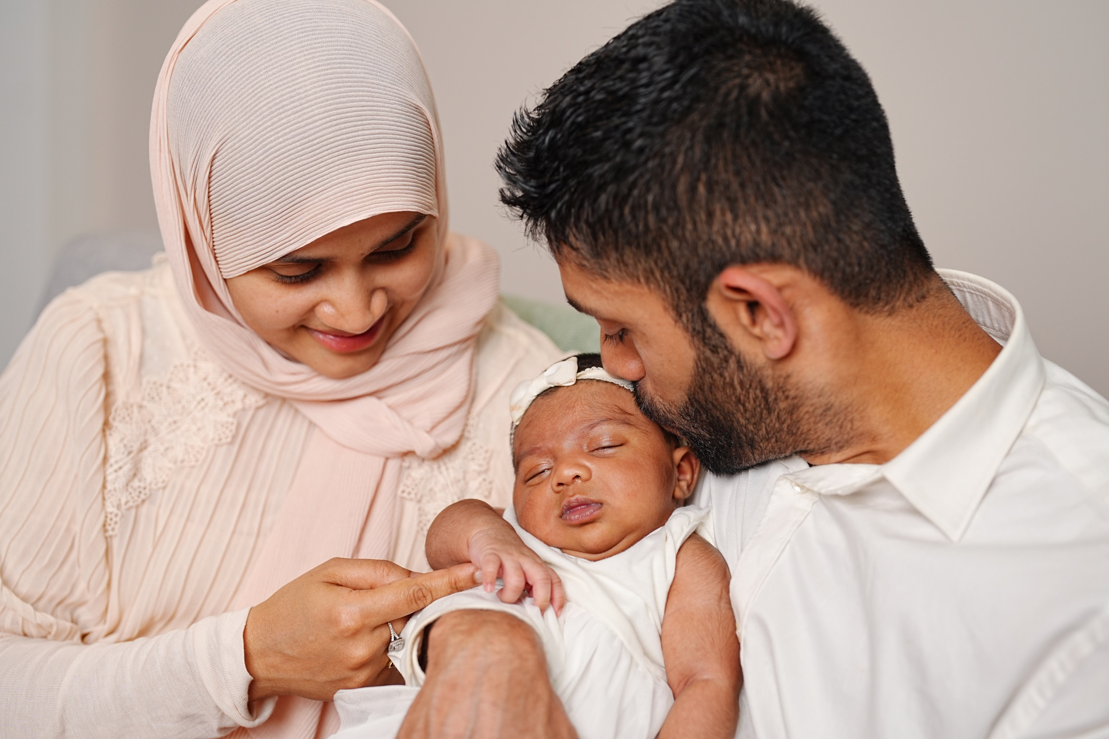Family with mother, father, and newborn baby, with the father gently kissing the baby's forehead.