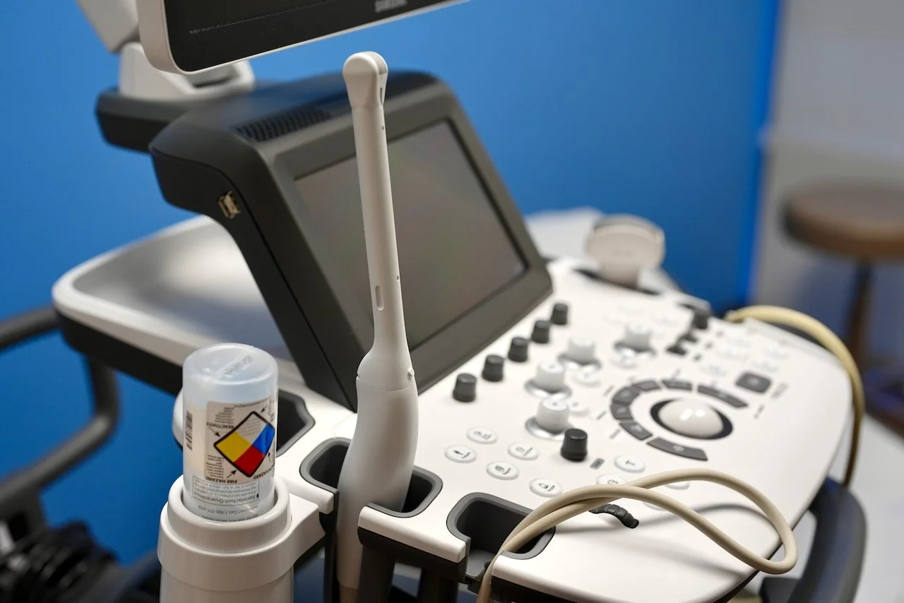 Medical ultrasound machine with control panel, screen, and probes in a clinical setting.