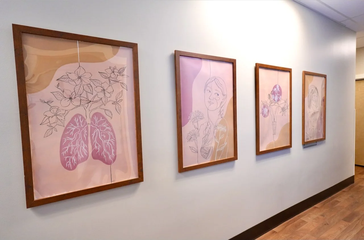 Four framed line art illustrations with floral and human face themes on a white wall in an indoor gallery or corridor.