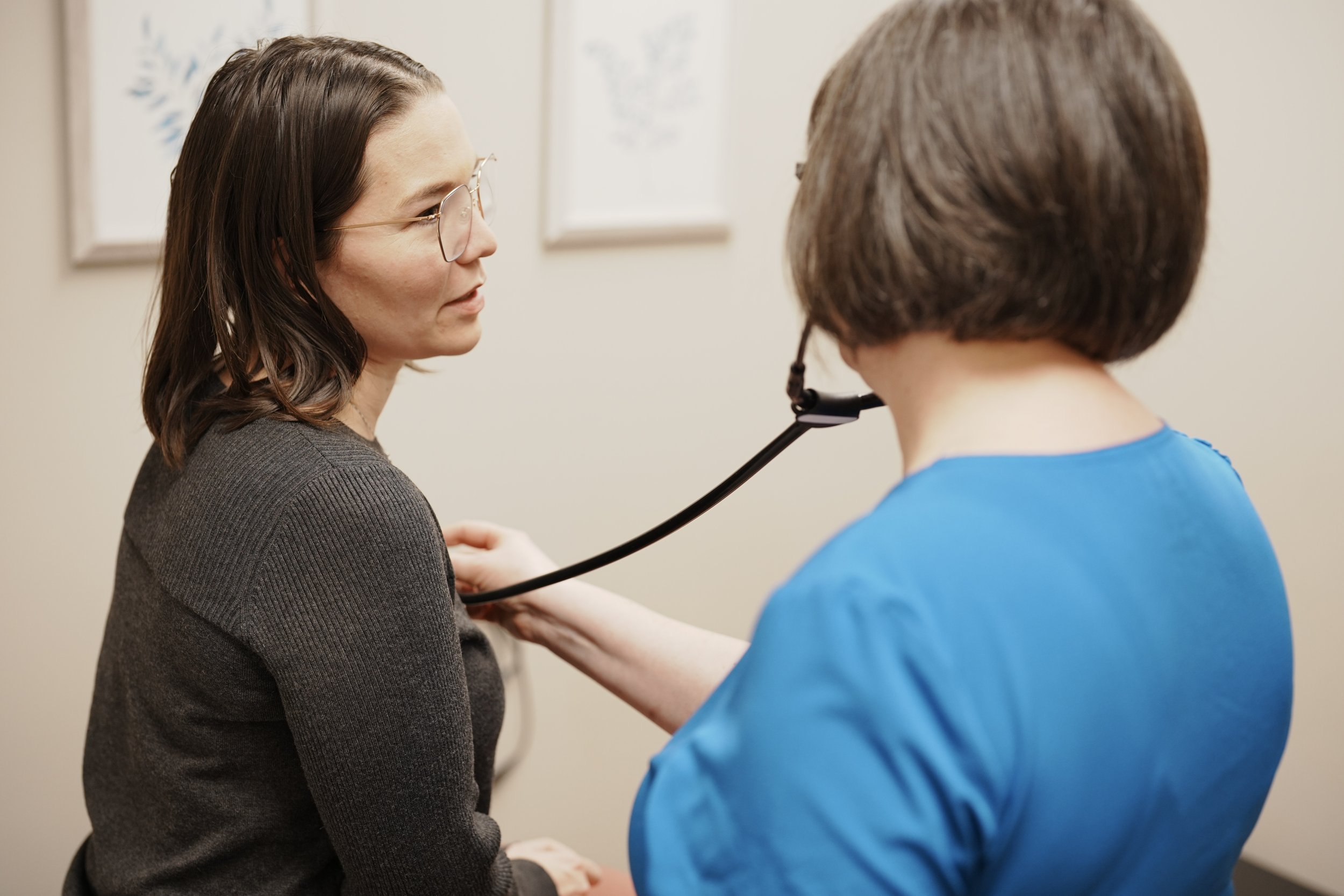 A healthcare professional using a stethoscope on a woman's chest during a medical examination.