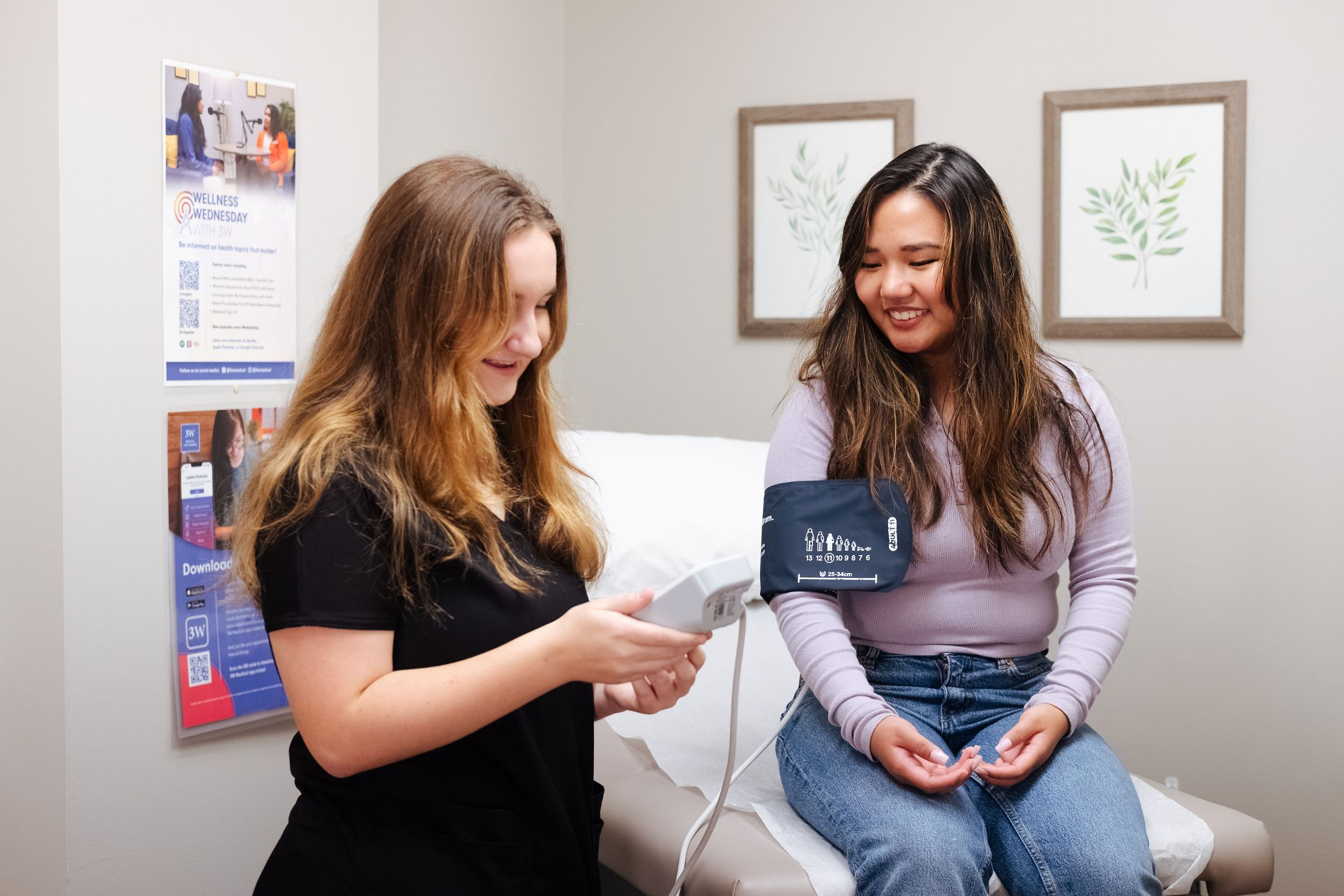 A healthcare professional taking a woman's blood pressure in a medical office, with informational posters on the wall.