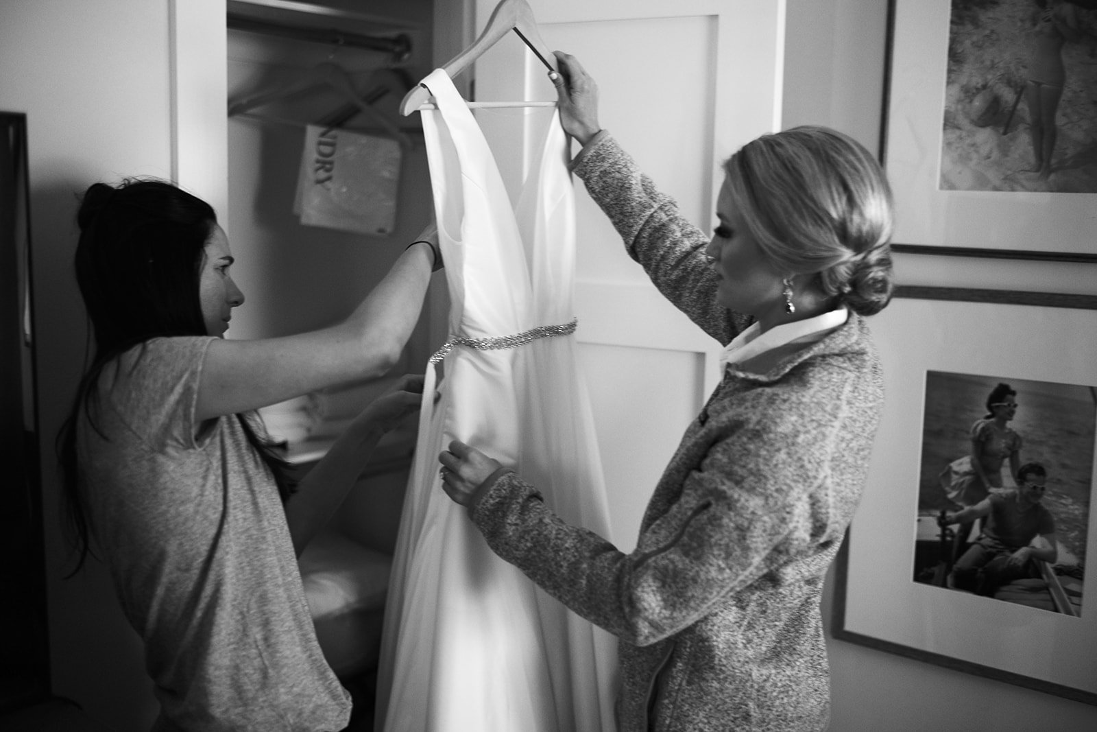 Two women are hanging a wedding dress in a bedroom.