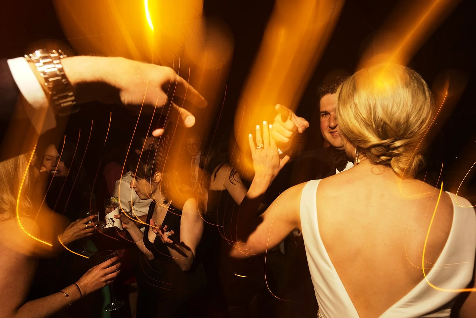 Couple dancing at a party or wedding reception with colorful light streaks in the background.