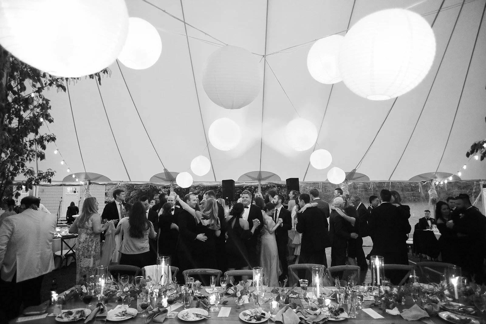 Wedding reception under a canopy with hanging lanterns, guests dancing and dining at tables.