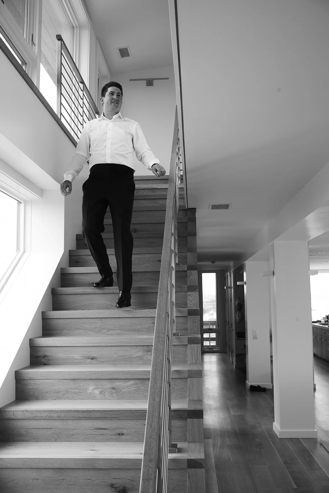 A man in a white shirt and black pants walking downstairs in a modern home.
