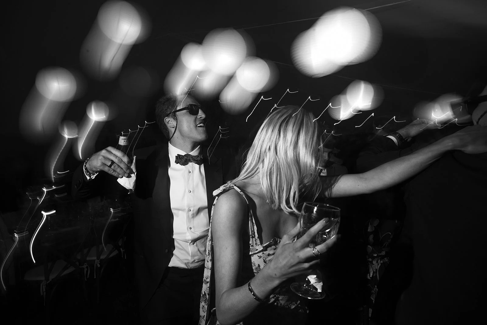 People dancing and enjoying drinks at a party, black and white photo with motion blur light streaks.