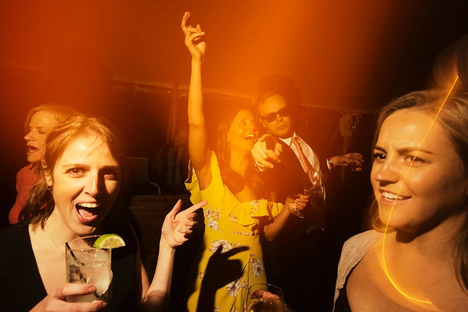 Group of people at a party dancing and drinking under orange lighting.