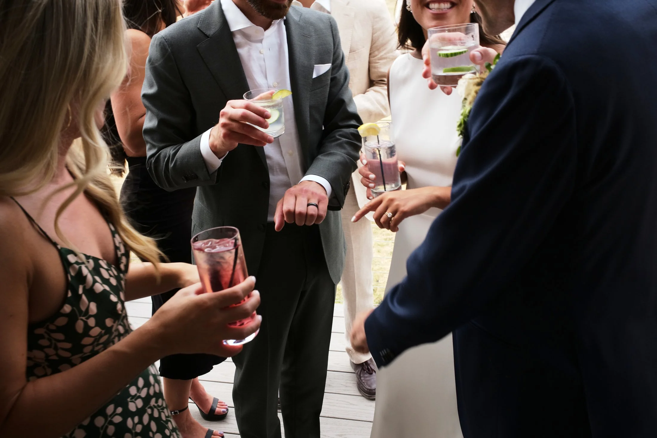 Group of people at a social gathering holding drinks, engaged in conversation, dressed in formal and semi-formal attire.