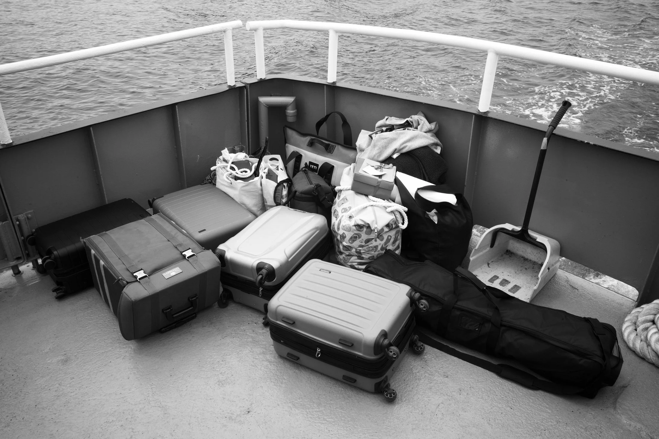 Luggage and bags on the deck of a boat with water in the background.