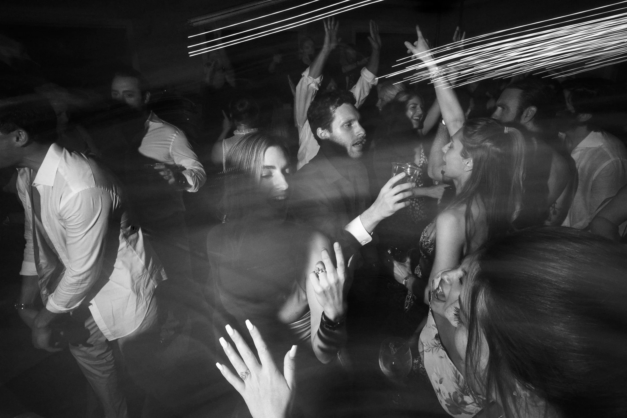 People dancing and socializing at a party, with motion blur and light streaks in black and white.