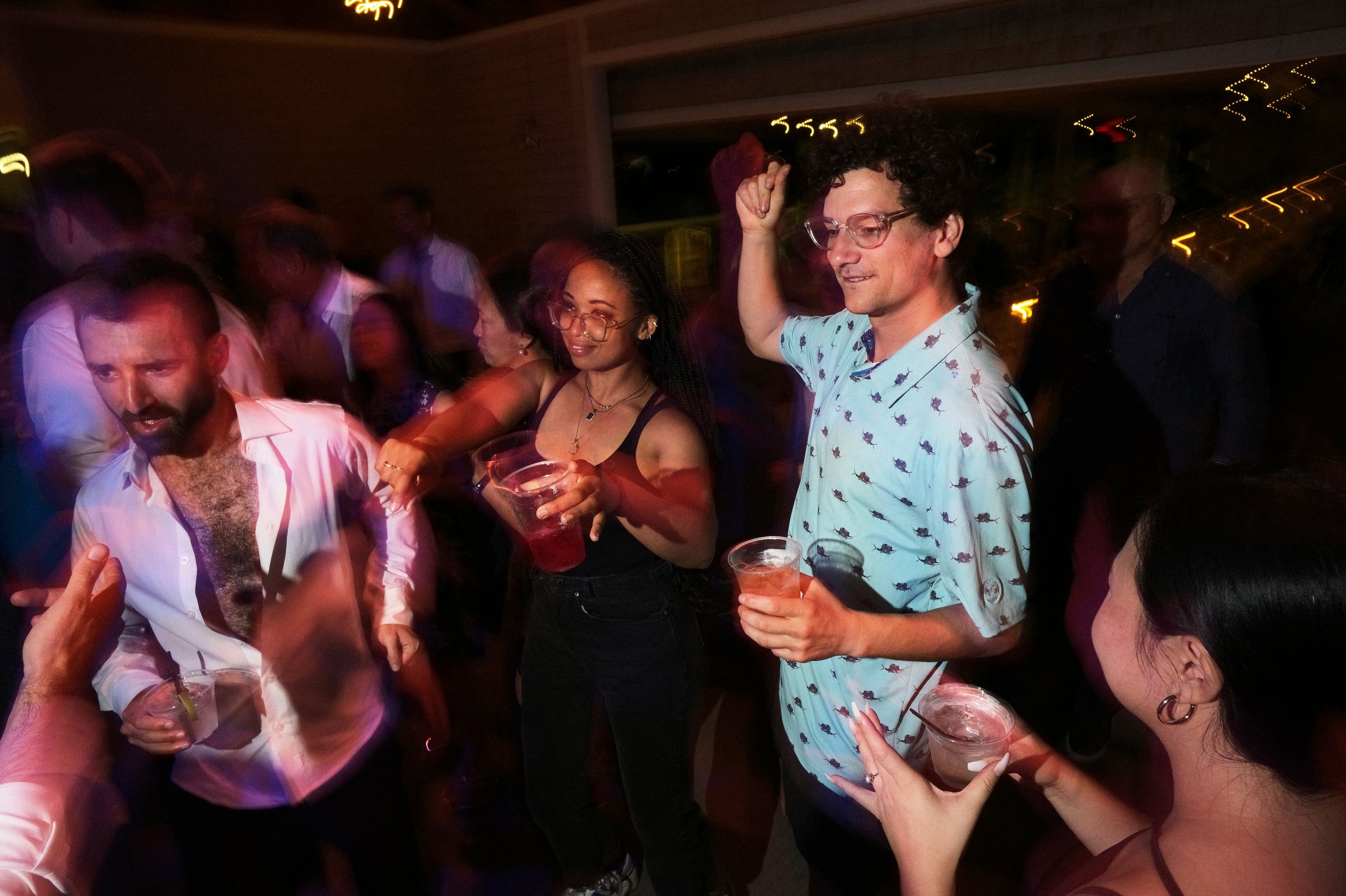 People dancing and socializing at a party with drinks in hand, in a dimly lit environment.