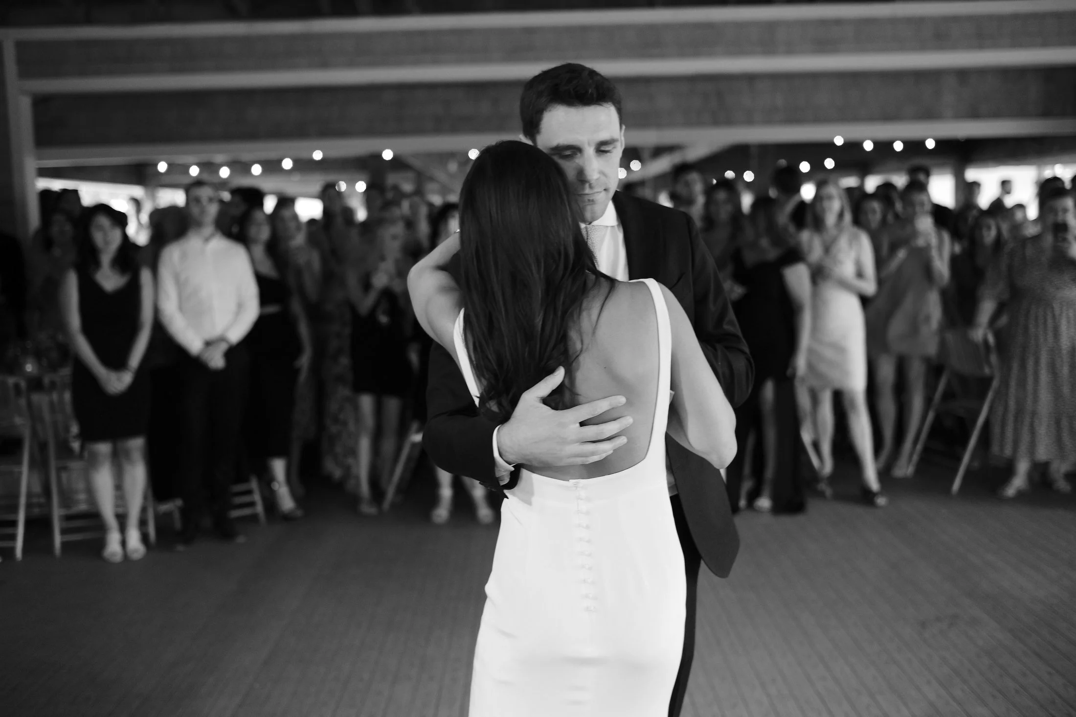 A couple dancing closely at a wedding reception, with guests watching in the background.